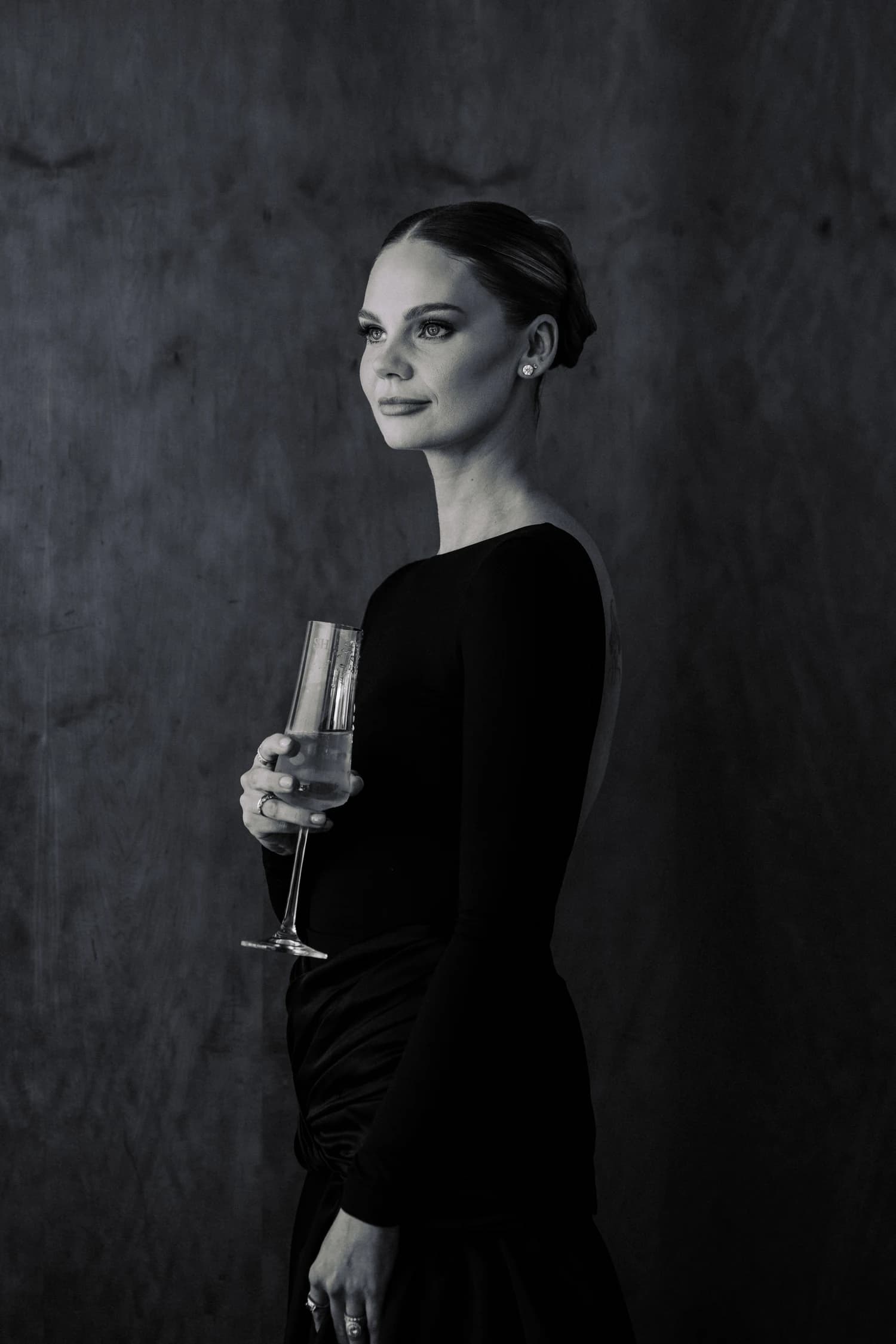 A woman in a fitted black evening gown holding a champagne flute.