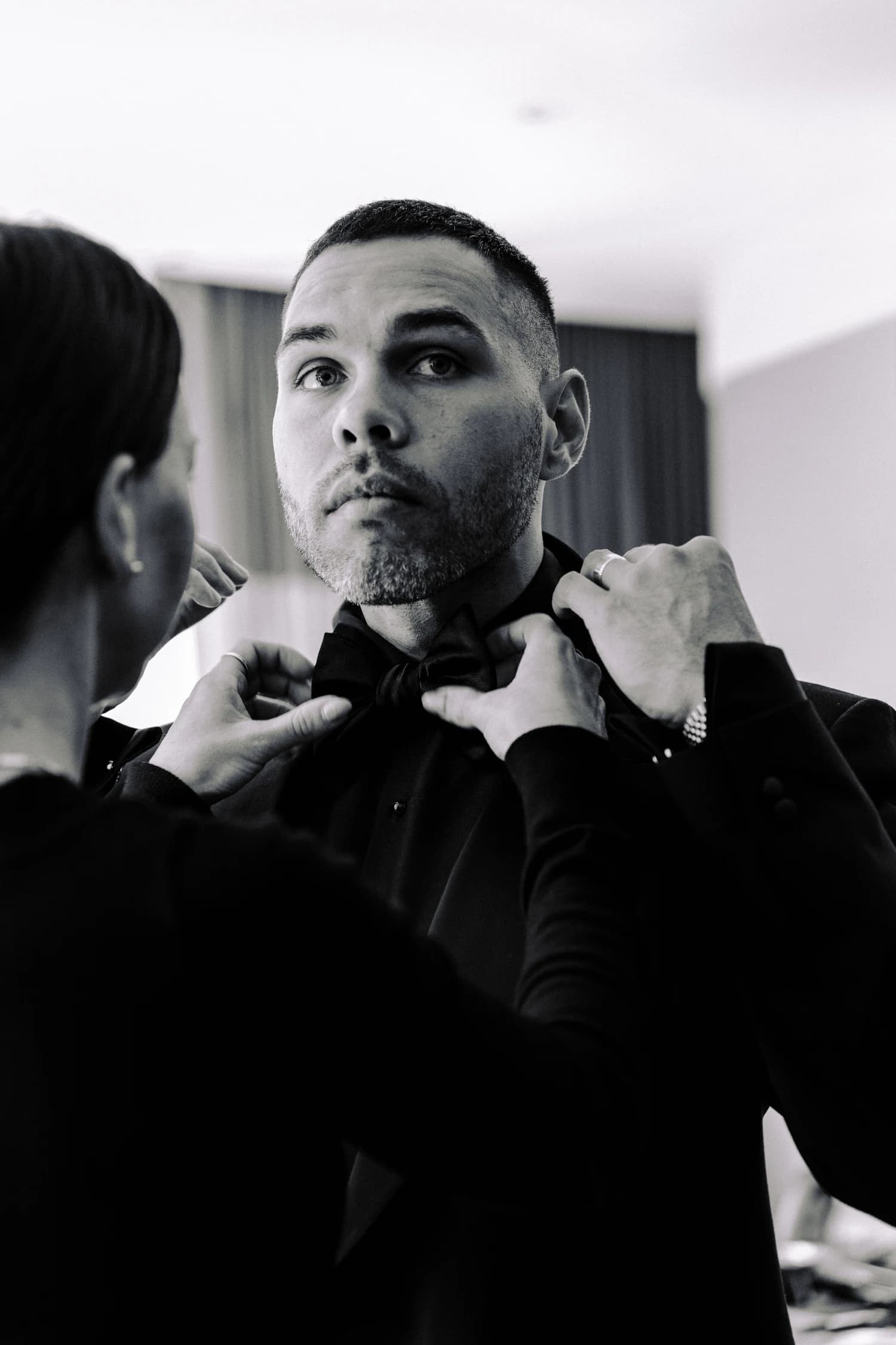 A bow tie being adjusted over a black shirt in the dressing room.