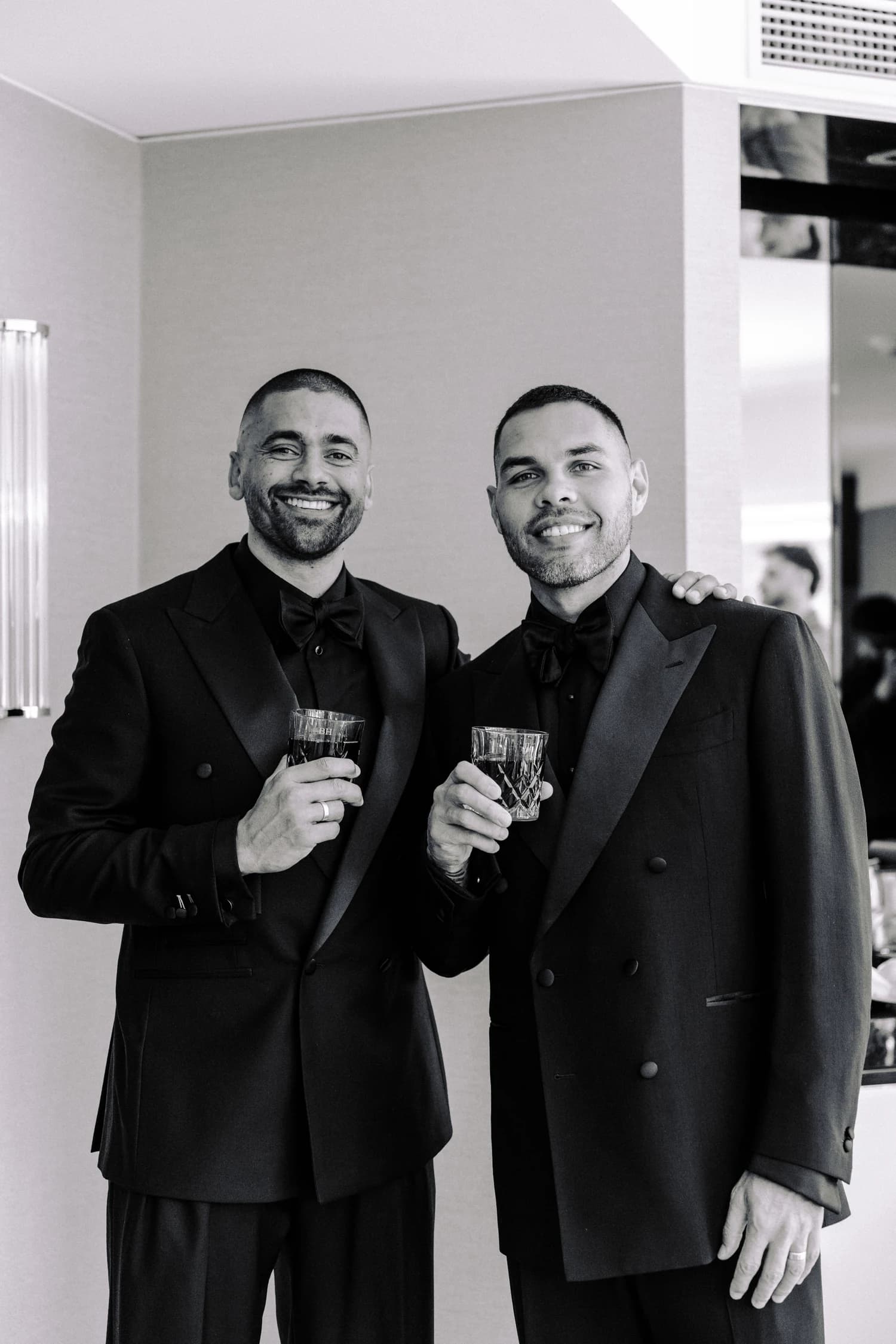 Two men smiling together in dark suits while holding glasses.