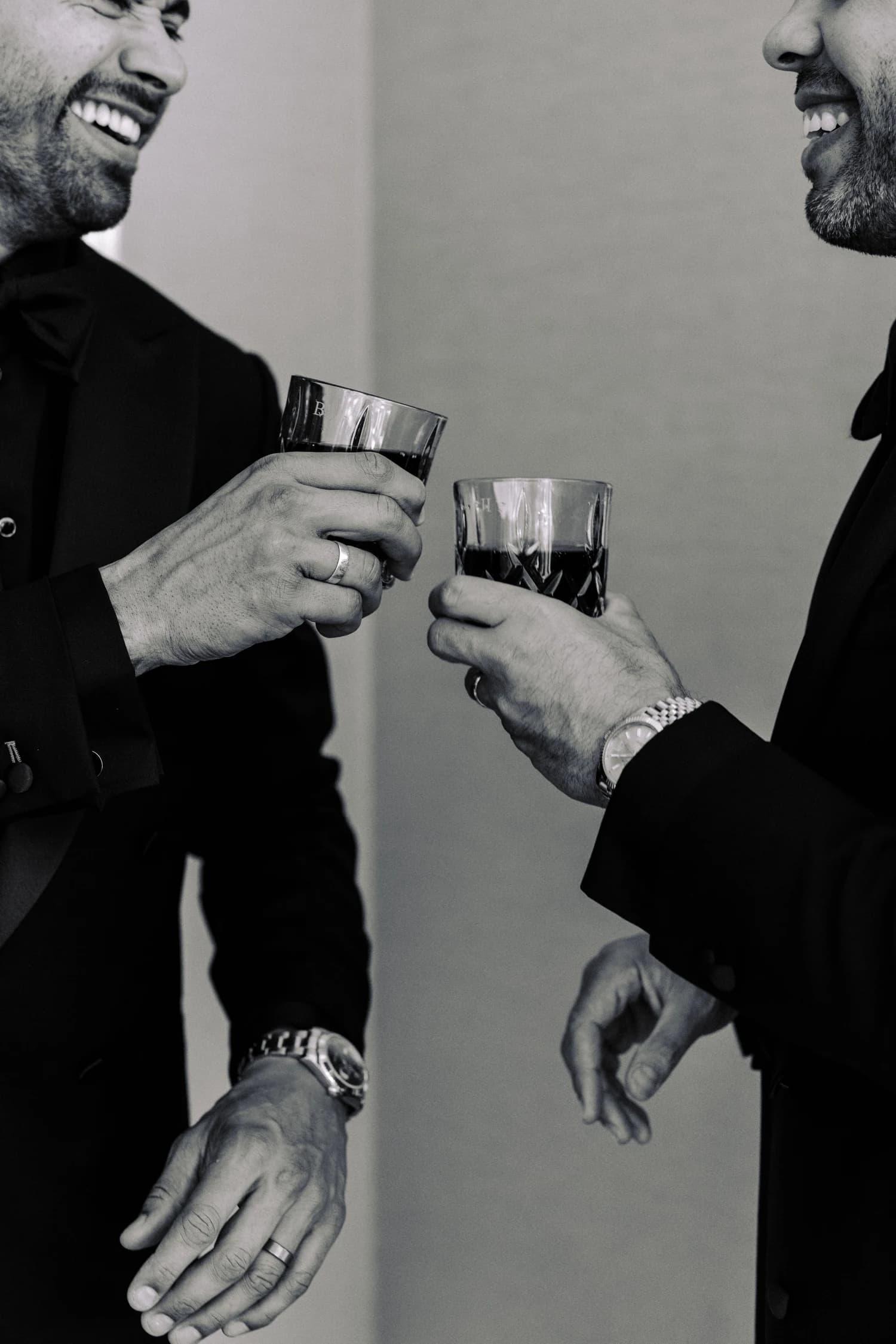 Two men in dark suits laughing together while holding cut-glass tumblers.