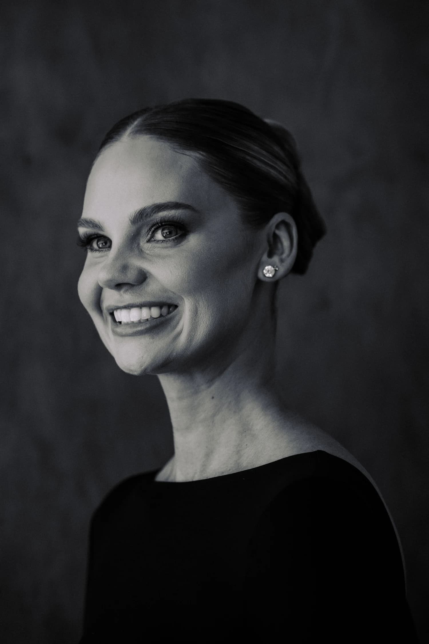 A close portrait of a woman in a black evening gown, with her hair swept back.