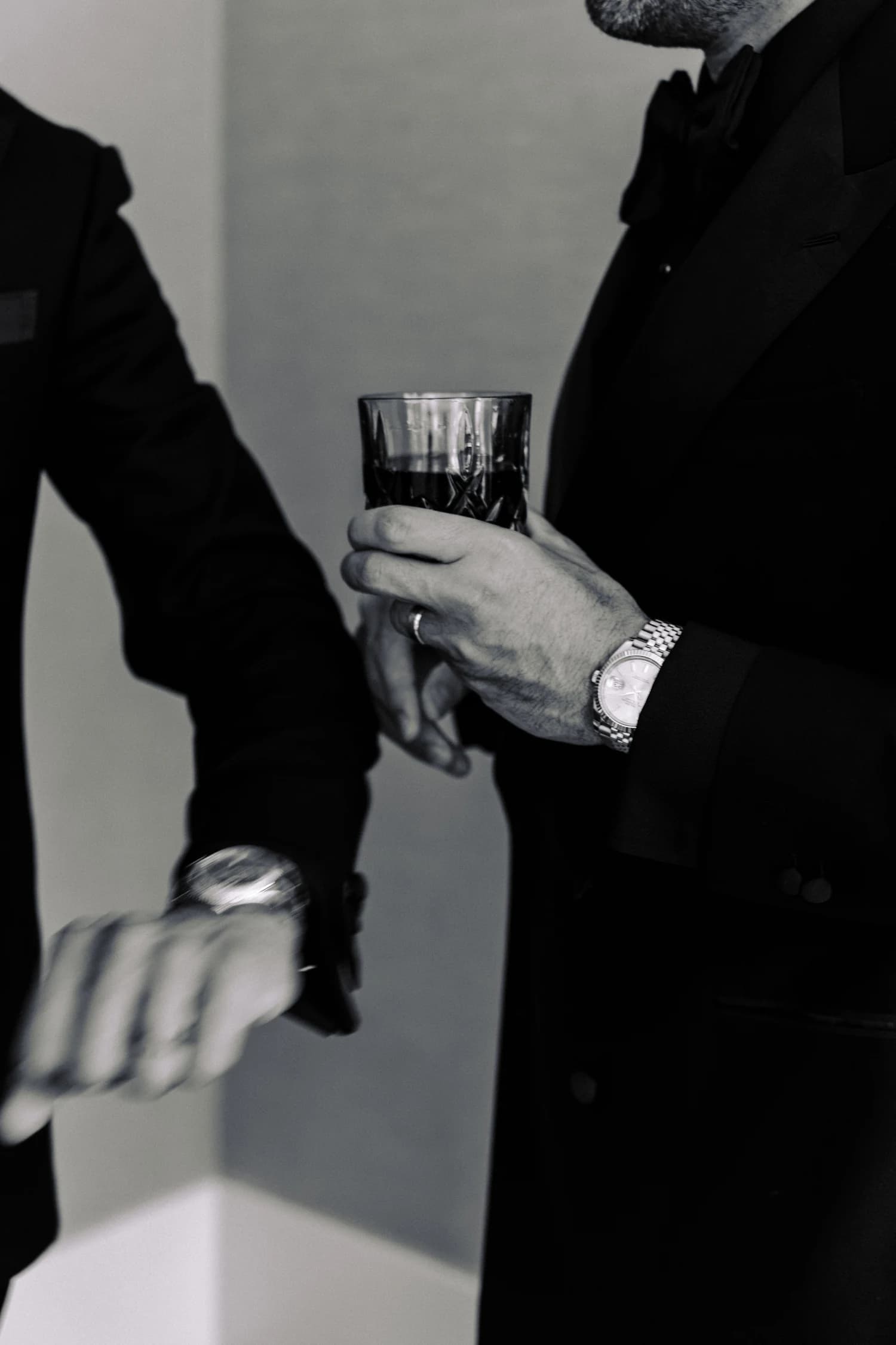 A close view of hands holding a cut-glass tumbler against a dark suit.