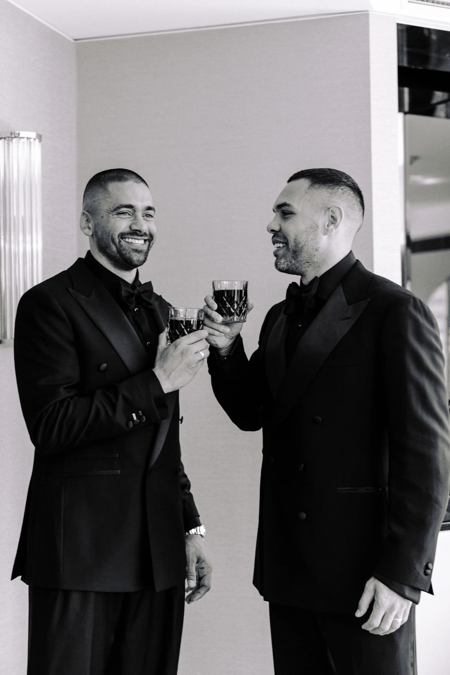 Two men in tailored suits raising cut-glass tumblers together.