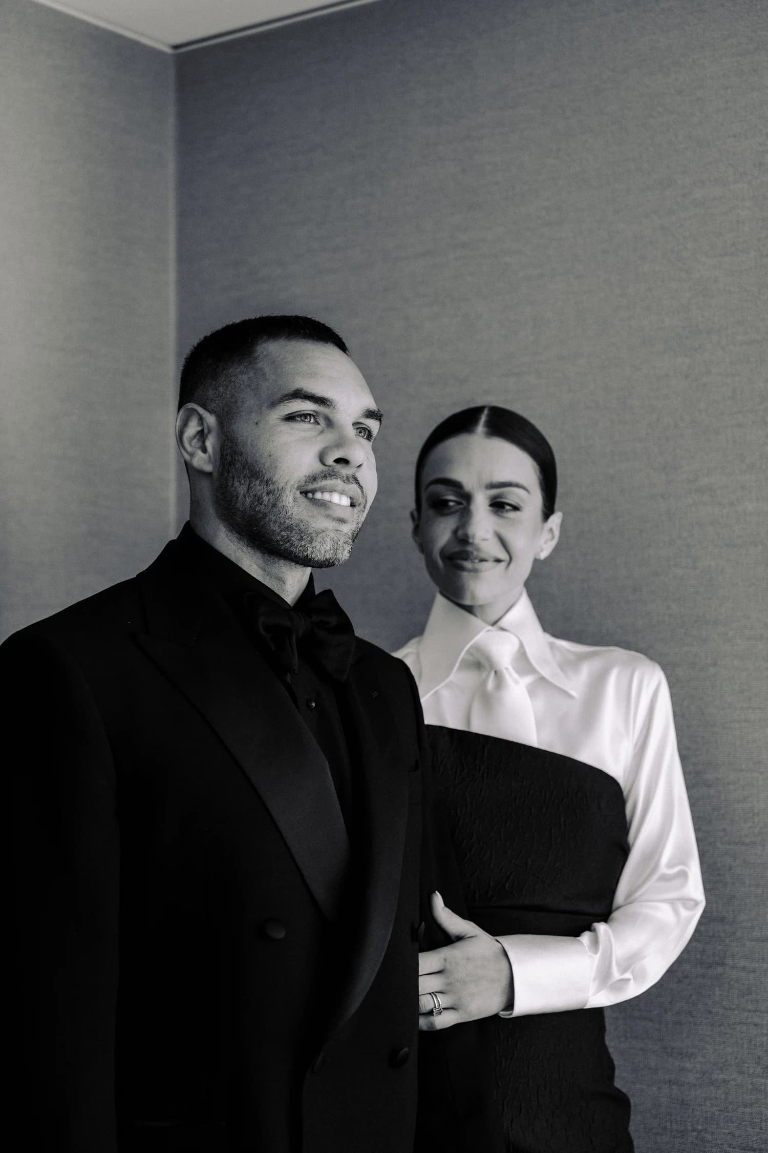 A man in a dark suit and a woman in a white blouse and black gown smiling together.