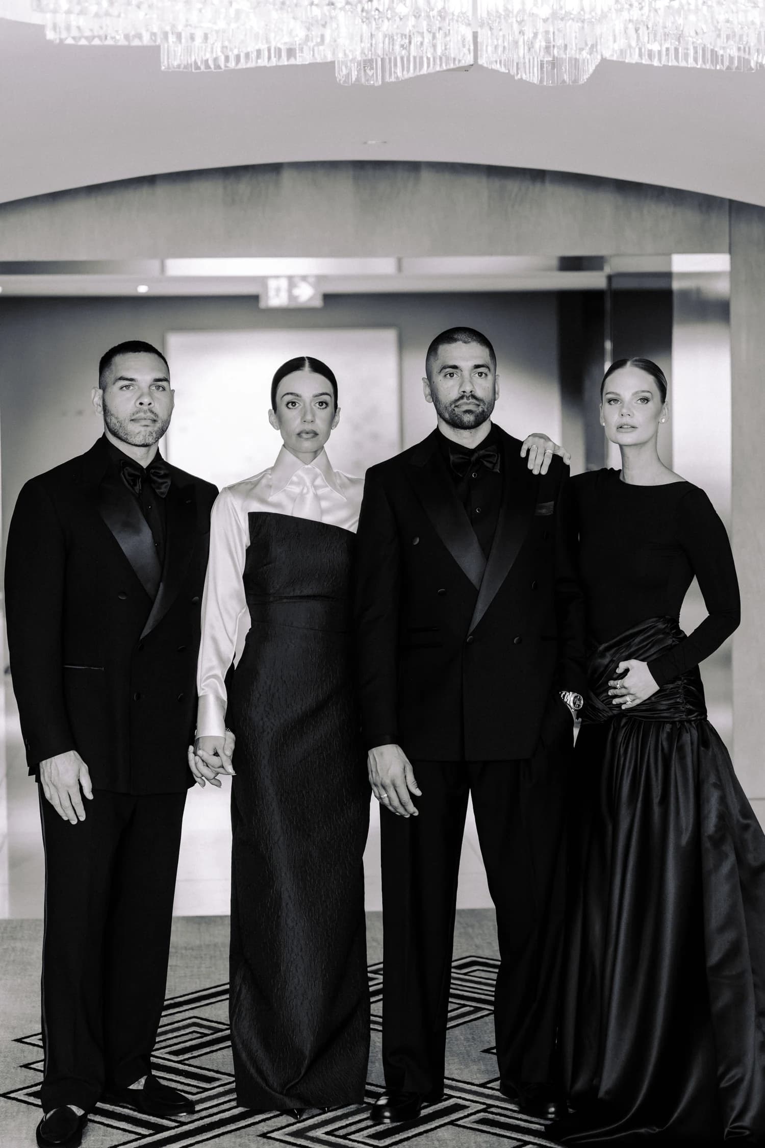 Two men in tailored suits and two women in evening gowns standing together at Crown Towers.
