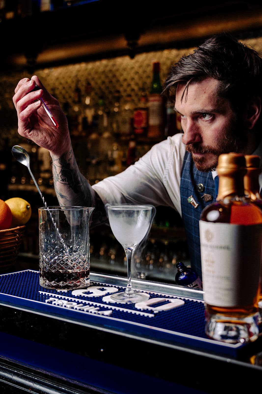 A bartender stirring a cocktail in a mixing glass across the bar