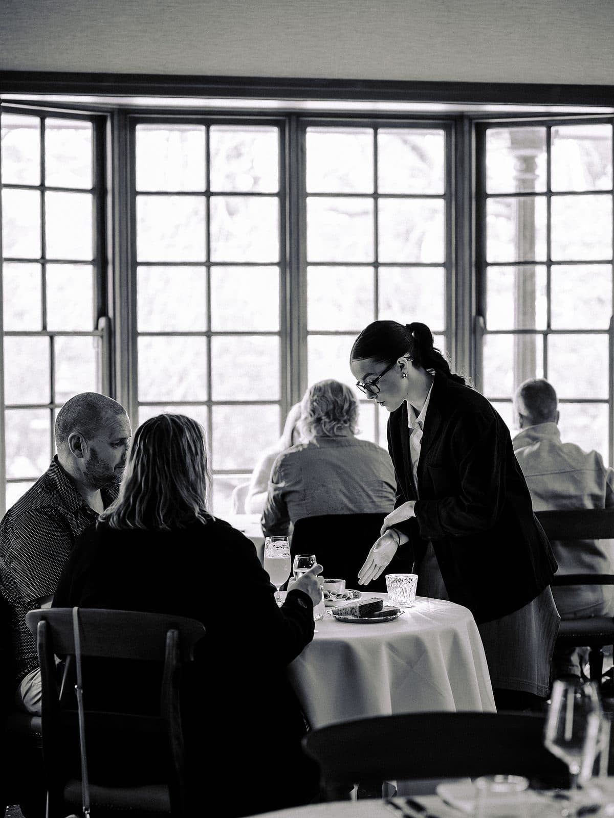 A waitress clearing a plate from a table beside a leadlight window