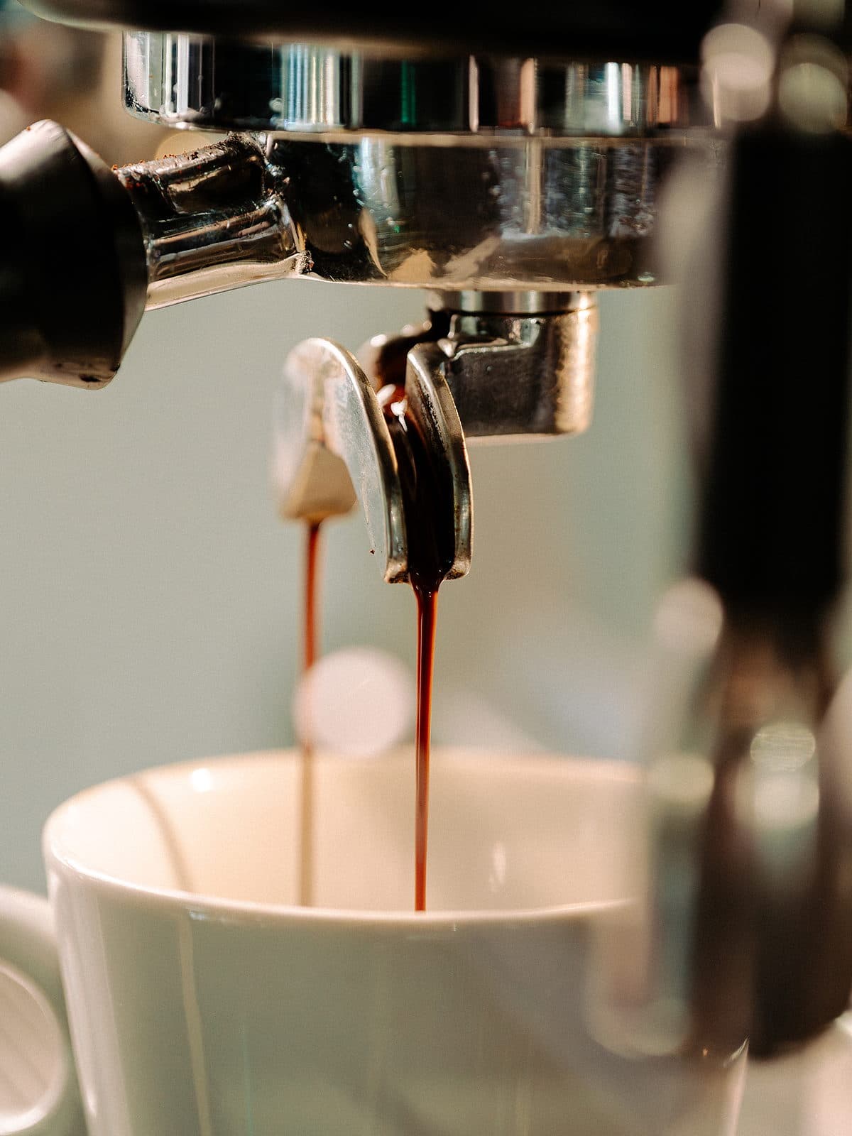 Espresso falling from a portafilter into a white cup