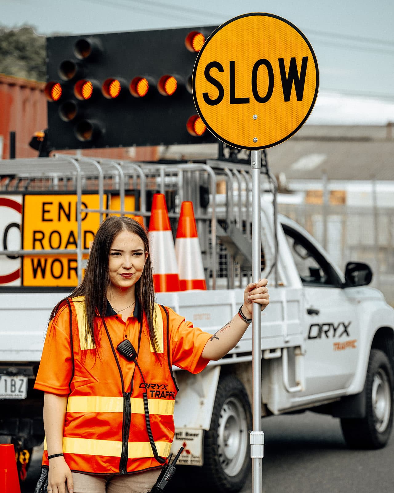 A traffic controller in hi-vis holding a slow sign beside a work ute