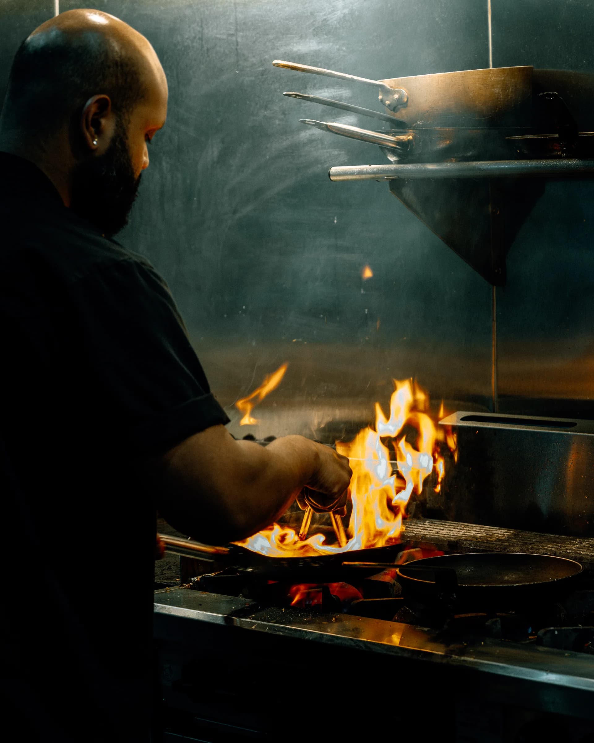 A chef cooking over a flaming pan in the Pearl by P&D kitchen