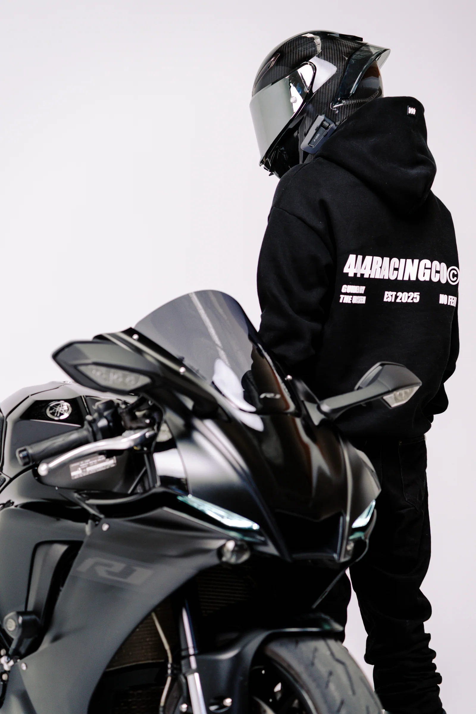 Rear view of a 444racingco hoodie showing its white back graphic beside a motorcycle