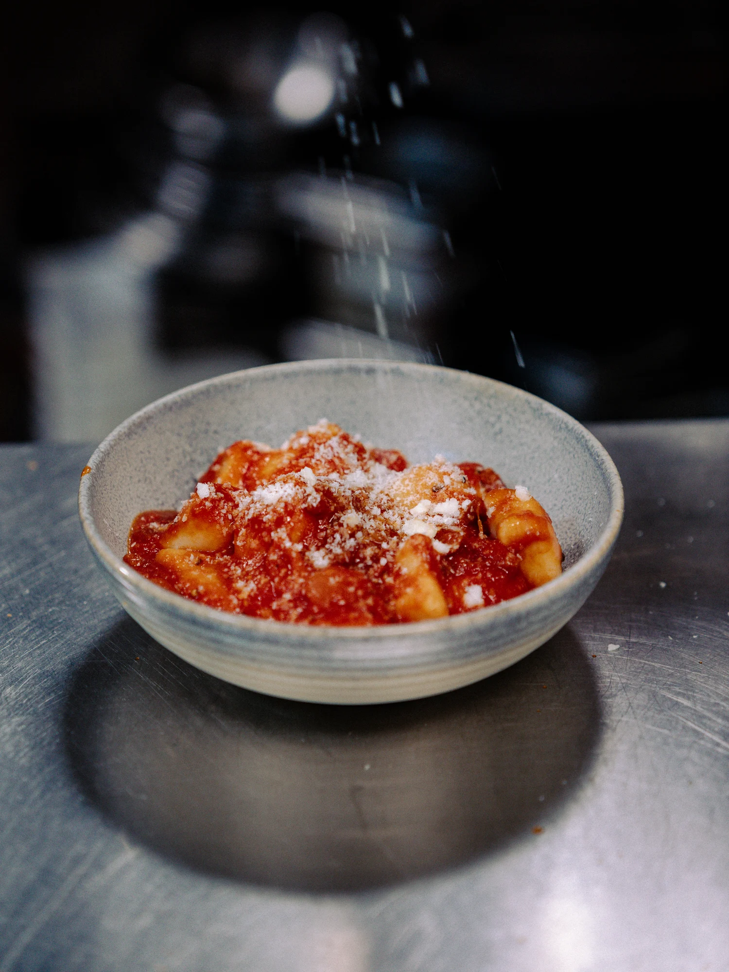 Cheese being grated over a bowl of gnocchi in tomato sauce at Circa 1884.