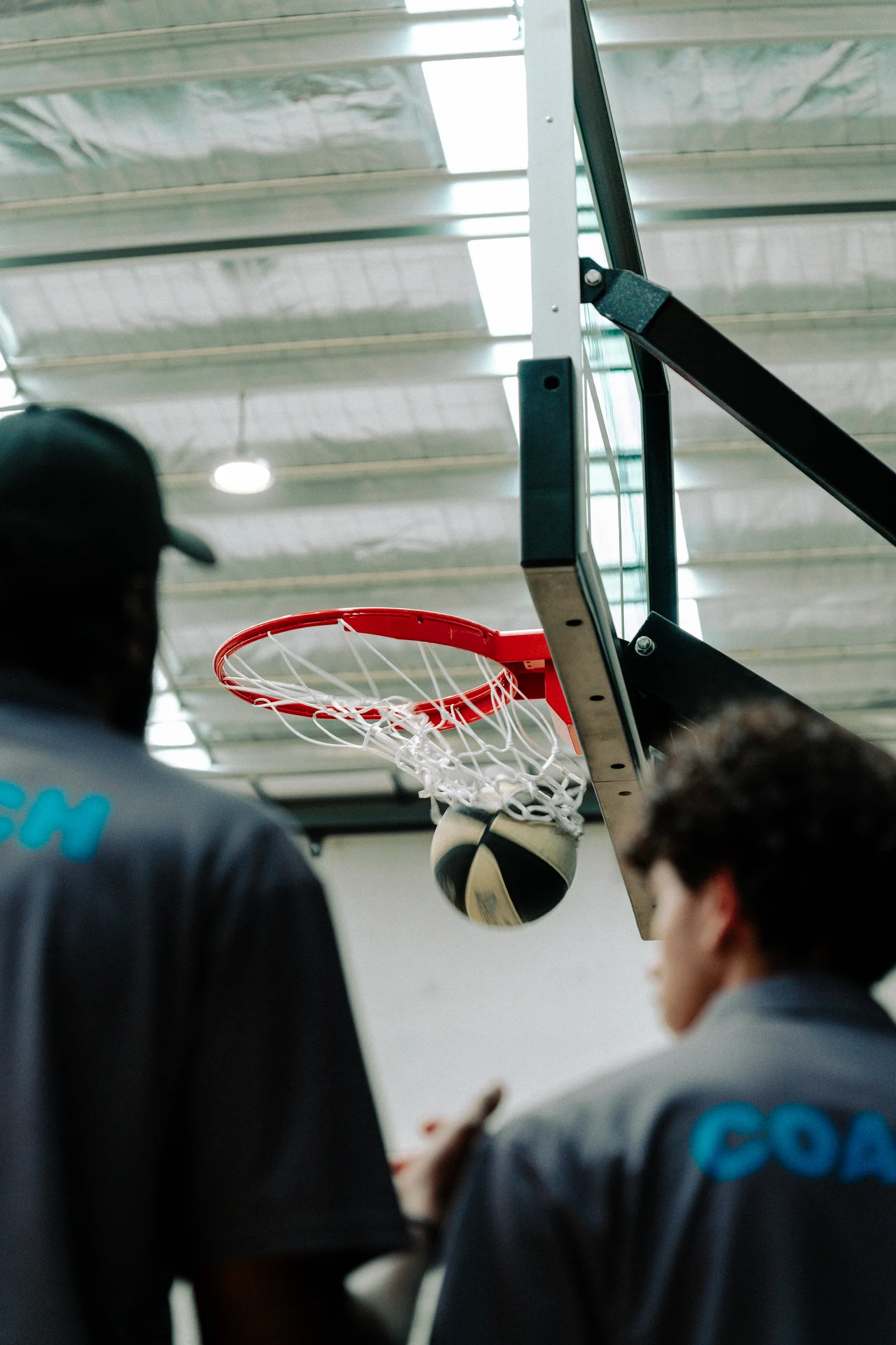 Rear view of two coaches watching a basketball at the hoop