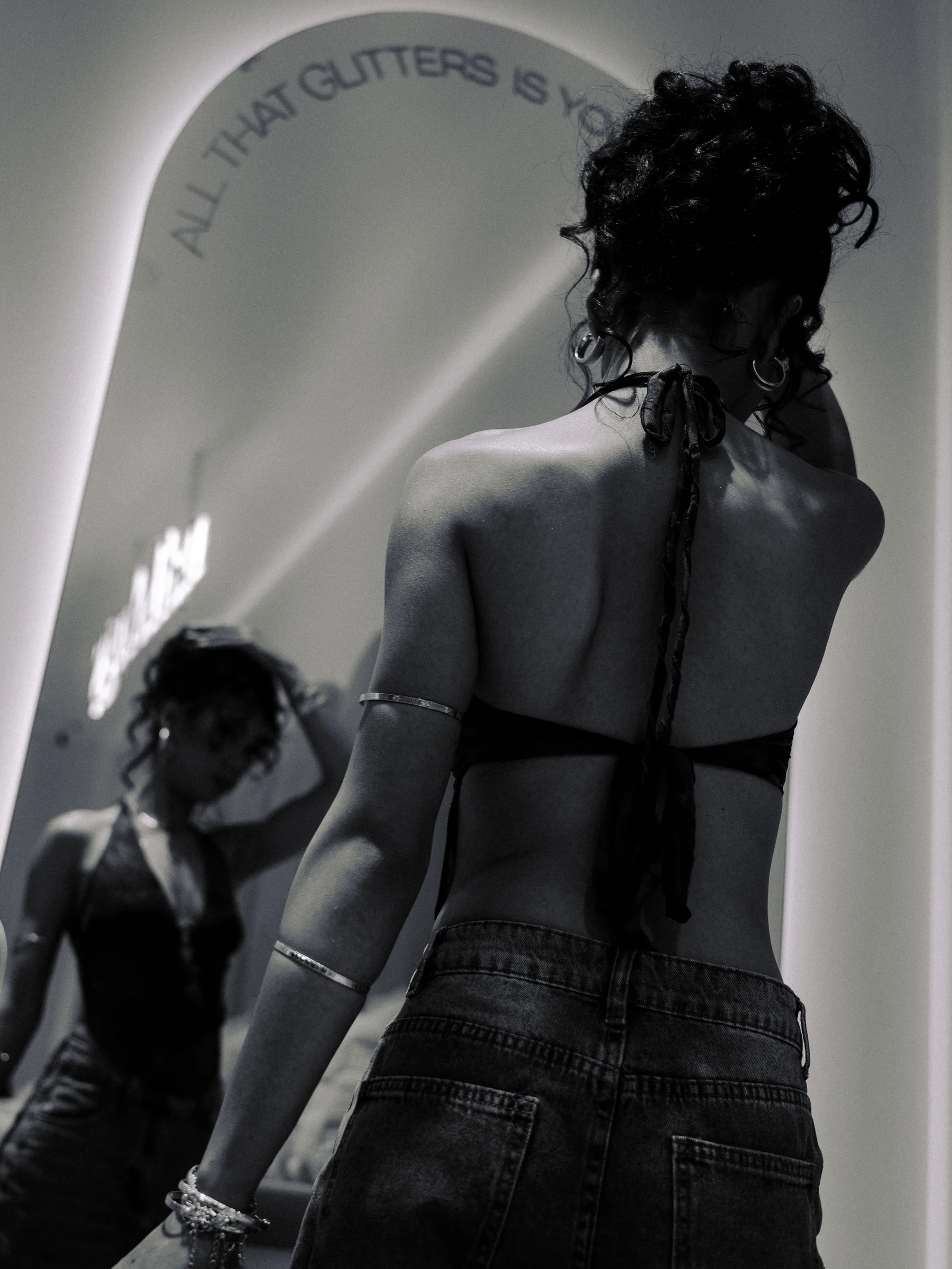 Black and white photograph of a model seen from behind with her reflection in a mirror